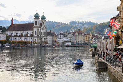 Boats in river by buildings in city against sky