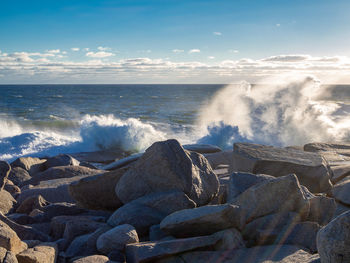 Waves splashing on rocks at shore against sky