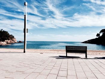 Bench on beach against sky