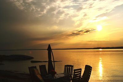 Table and chairs arranged at sea shore during sunset