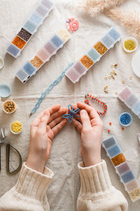 A beaded butterfly in the hands of a girl and items for beadwork on the table. 