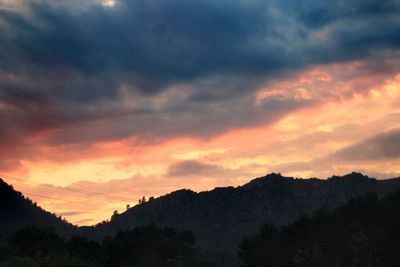 Silhouette trees against dramatic sky during sunset