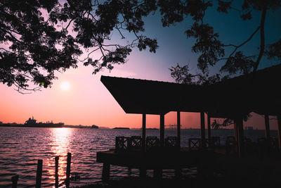 Silhouette built structure by lake against sky during sunset