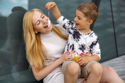 Happy blond woman and little boy sitting on terrace and eating sweets. mother and son enjoy