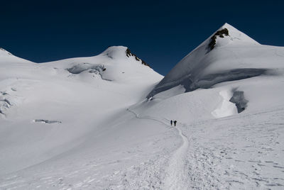 Low angle view of snowcapped mountains against clear blue sky