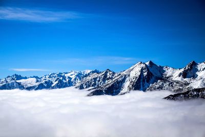 Scenic view of snowcapped mountains and clouds against blue sky on sunny day