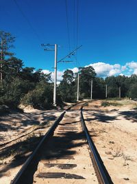 Railroad tracks by trees against blue sky