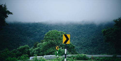 Yellow road sign on mountain against sky