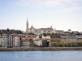 Buildings by river against sky in city