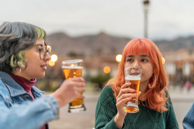 Delighted youth women sitting at table in veranda of pub in city of cusco and drinking glass of beer