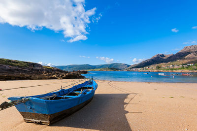 Boats moored on beach against blue sky