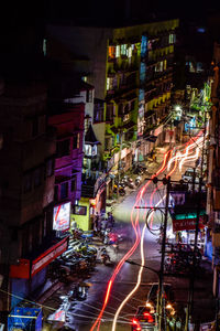 Light trails on city street amidst buildings at night