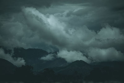 Low angle view of storm clouds over silhouette mountain