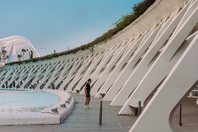 Rear view of woman standing by swimming pool against sky