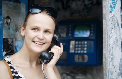 Happy young woman talking on pay phone