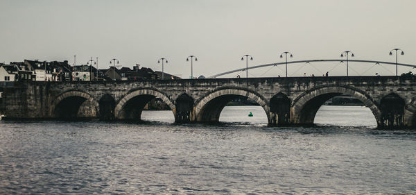 Arch bridge over river against sky in city