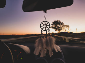 Close-up of dreamcatcher hanging on rear-view mirror of car during sunset