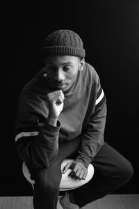 Portrait of young man sitting against black background