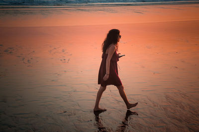 Side view of woman standing on beach during sunset