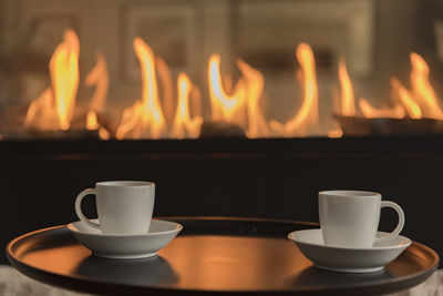 Close-up of coffee cups in tray against fireplace