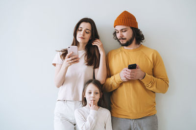 Young family with child little girl on the gray wall background, parents using mobile phones