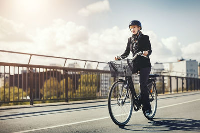 Man riding bicycle on bridge in city against sky