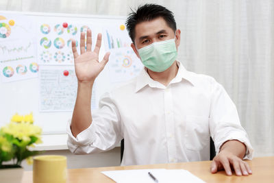 Portrait of man wearing mask gesturing while sitting in office