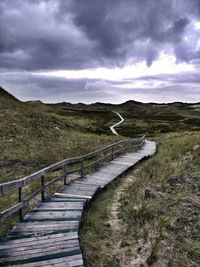 Footpath leading towards landscape against sky