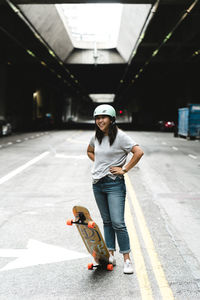 Smiling woman with skateboard looking away while standing in parking lot