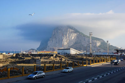 Cars moving on road by mountain against cloudy sky