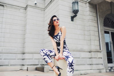 Full length of woman sitting on bollard against building