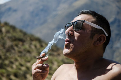 Man smoking marijuana joint while wearing sunglasses against mountains