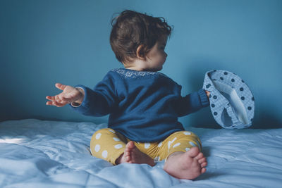 Baby girl holding cap while sitting on bed at home