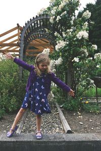 Full length of girl with arms outstretched standing on retaining wall