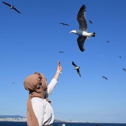 Young woman feeding birds against sky