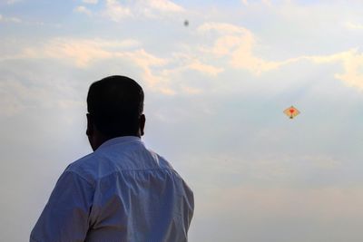 Rear view of man flying kite against sky