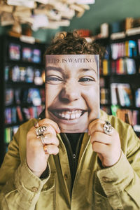 Young man holding book in front of face in bookstore