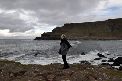 Woman standing on seashore at giants causeway against sky