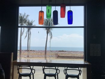 Chairs and table by sea against sky seen through glass window