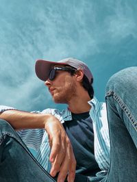 Low angle view of man in sunglasses sitting against blue sky