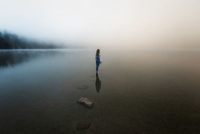 Young blonde girl standing in the foggy lake at sunrise in the wilderness forest.	