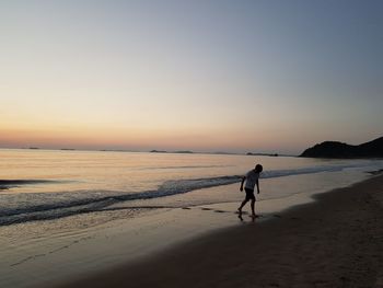 Man walking on beach against sky during sunset