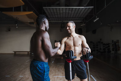 Smiling young sports people with barbell shaking hands in gym