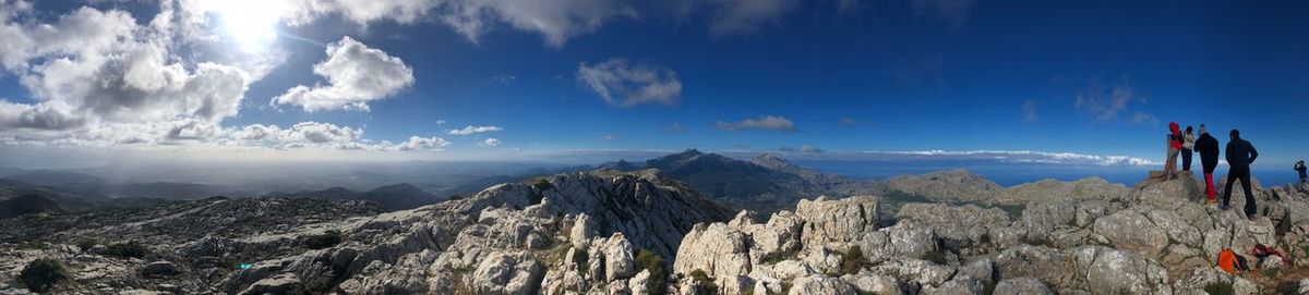 Panoramic view of mountains against sky with people standing on rock