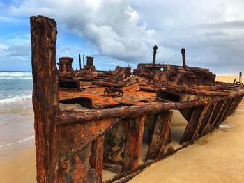 Old rusty metallic structure on beach against sky