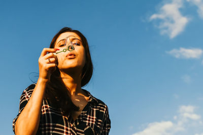 Low angle portrait of woman holding ice cream against sky