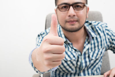 Portrait of mid adult man showing thumbs up while sitting on chair