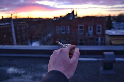 Midsection of person holding cigarette against sky in city
