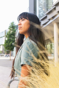 Side view of unemotional young ethnic female in stylish clothes looking away standing against pampas bush on sunny summer day in park