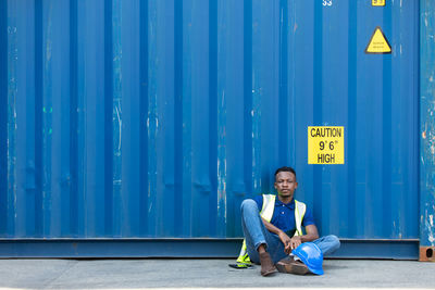 Portrait of young man sitting against blue wall